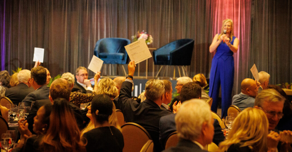 Nonprofit gala guests raising paddles during a Fund-A-Need fundraising appeal.