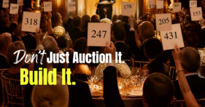 Guests raise bid paddles during a nonprofit live auction with the message “Don’t Just Auction It. Build It.”